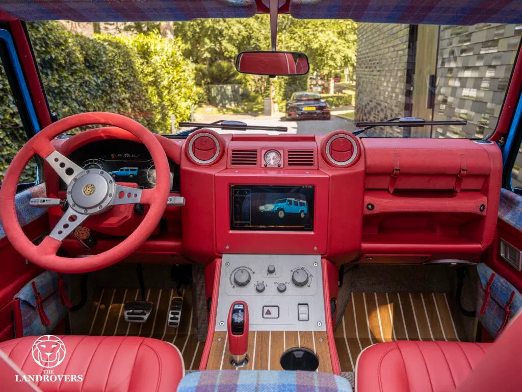 Central touchscreen in the red Strawberry Fields Forever dashboard, showing a blue vehicle and control sidebar.